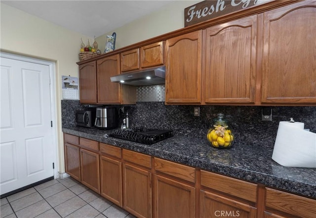 kitchen featuring black gas stovetop, light tile patterned floors, backsplash, and dark stone countertops