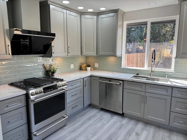 kitchen featuring gray cabinets, appliances with stainless steel finishes, sink, light stone countertops, and wall chimney exhaust hood