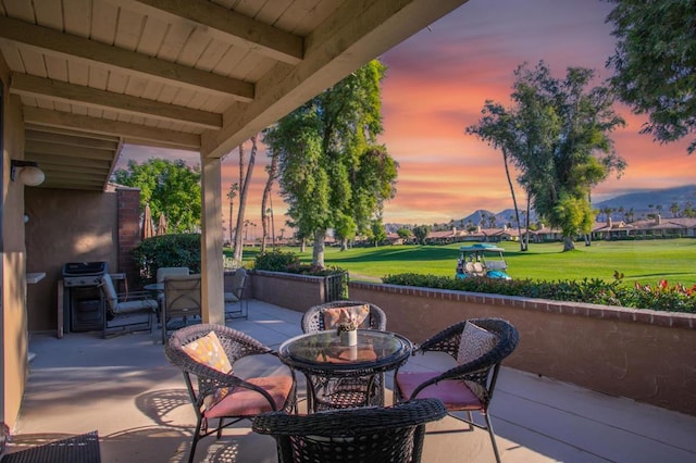 patio terrace at dusk featuring a grill and a lawn