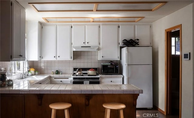 kitchen with stove, kitchen peninsula, white fridge, and white cabinetry