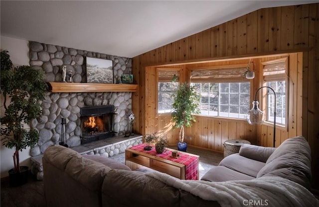 living room with wood walls, a stone fireplace, and vaulted ceiling