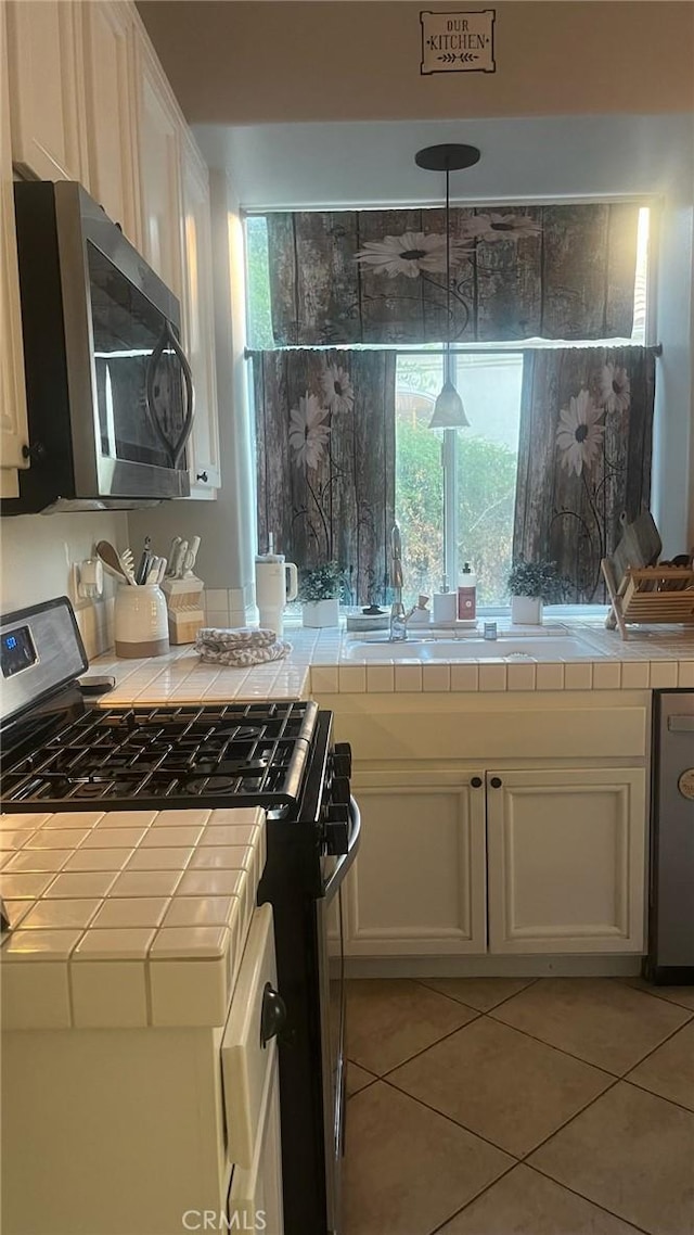 kitchen featuring white cabinets, appliances with stainless steel finishes, light tile patterned flooring, and tile countertops