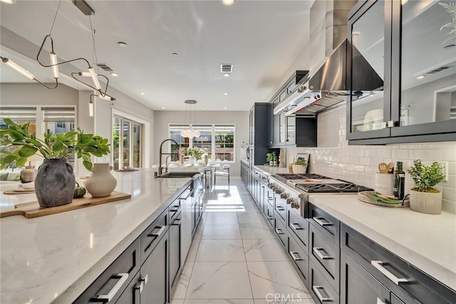 kitchen with decorative light fixtures, light stone countertops, range hood, and decorative backsplash