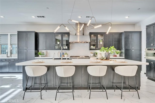 kitchen with extractor fan, stainless steel oven, a large island with sink, a kitchen breakfast bar, and backsplash