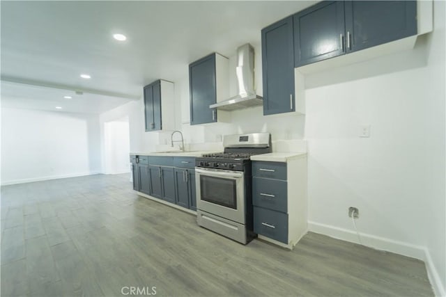 kitchen featuring wall chimney exhaust hood, stainless steel range with gas stovetop, sink, and hardwood / wood-style floors