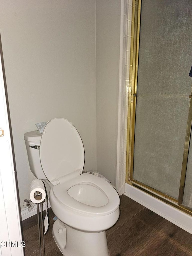 bathroom with wood-type flooring, toilet, and a shower with door