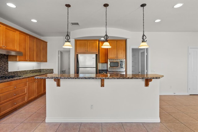 kitchen with stainless steel appliances, a kitchen island, dark stone countertops, and a kitchen breakfast bar