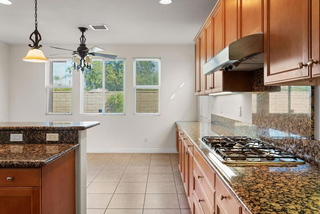 kitchen with light tile patterned floors, dark stone countertops, pendant lighting, ceiling fan, and stainless steel gas stovetop