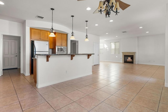 kitchen featuring fridge, a kitchen breakfast bar, stainless steel microwave, light tile patterned flooring, and dark stone counters