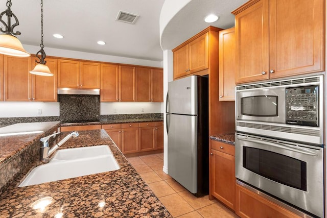 kitchen featuring sink, decorative light fixtures, light tile patterned floors, appliances with stainless steel finishes, and dark stone counters