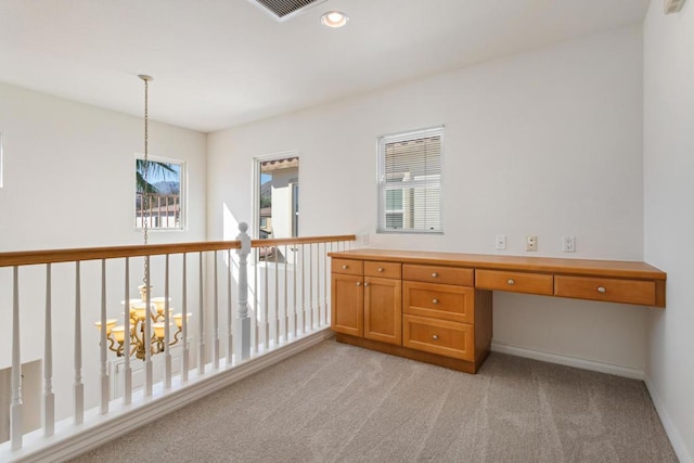 unfurnished office with light carpet, built in desk, and a chandelier