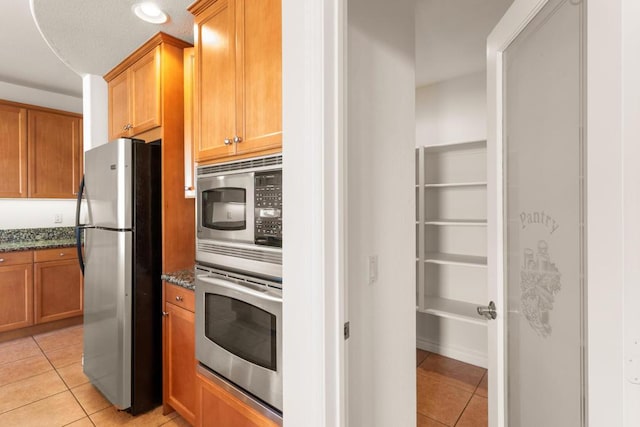 kitchen with light tile patterned flooring, appliances with stainless steel finishes, and dark stone countertops