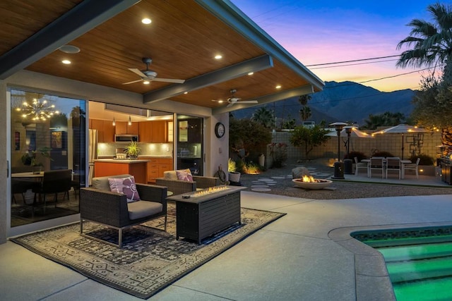 patio terrace at dusk featuring a mountain view, ceiling fan, and an outdoor living space with a fire pit