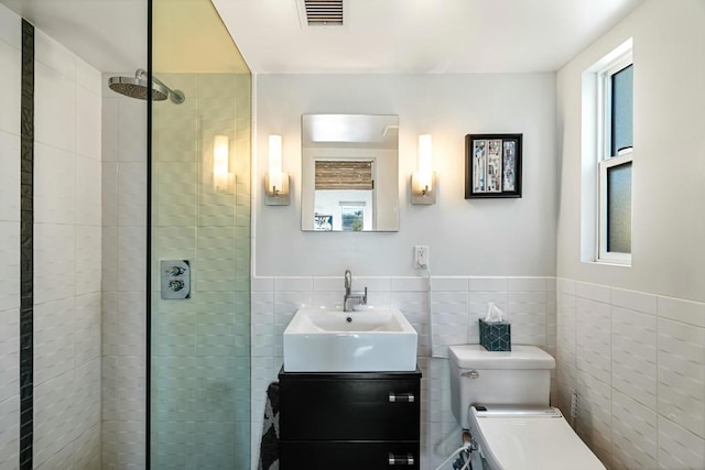 bathroom with toilet, vanity, tile walls, and a tile shower