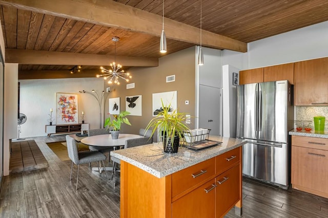 kitchen featuring decorative light fixtures, light stone counters, beamed ceiling, and stainless steel refrigerator