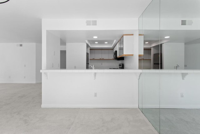 kitchen with fridge, light colored carpet, kitchen peninsula, and white cabinets