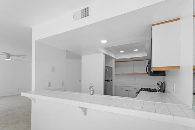 kitchen featuring stainless steel fridge, range, tile counters, white cabinets, and kitchen peninsula