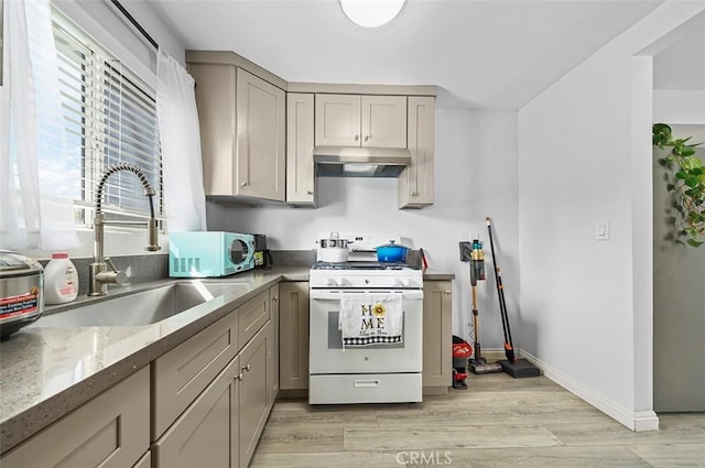 kitchen featuring gray cabinetry, light wood-type flooring, white gas stove, light stone counters, and sink