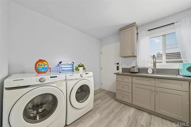 washroom featuring cabinets, sink, washing machine and clothes dryer, and light hardwood / wood-style floors