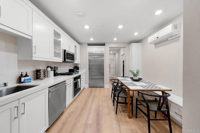 kitchen featuring light wood-type flooring, an AC wall unit, stainless steel appliances, and white cabinetry