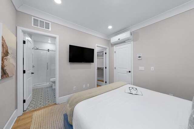 bedroom featuring a spacious closet, light hardwood / wood-style floors, a wall unit AC, connected bathroom, and a closet