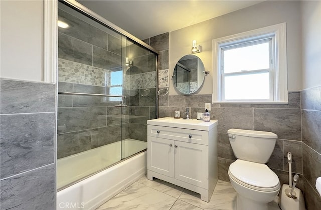 full bathroom with bath / shower combo with glass door, toilet, vanity, and tile walls