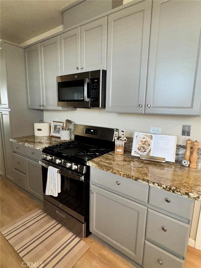 kitchen featuring light hardwood / wood-style floors, appliances with stainless steel finishes, gray cabinetry, and dark stone counters