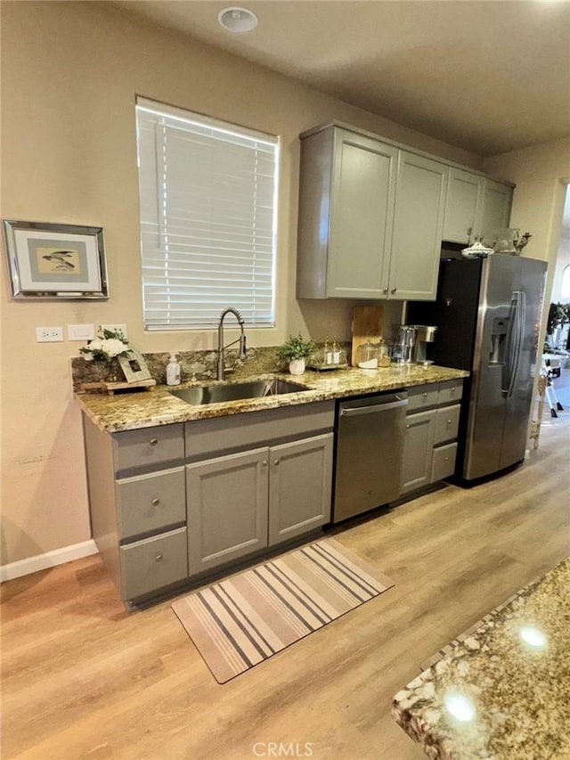 kitchen featuring stainless steel appliances, light hardwood / wood-style floors, light stone counters, and sink