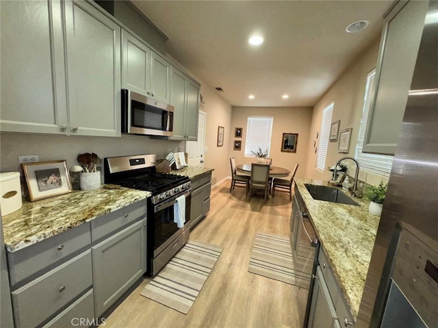 kitchen with appliances with stainless steel finishes, light hardwood / wood-style floors, light stone counters, and sink