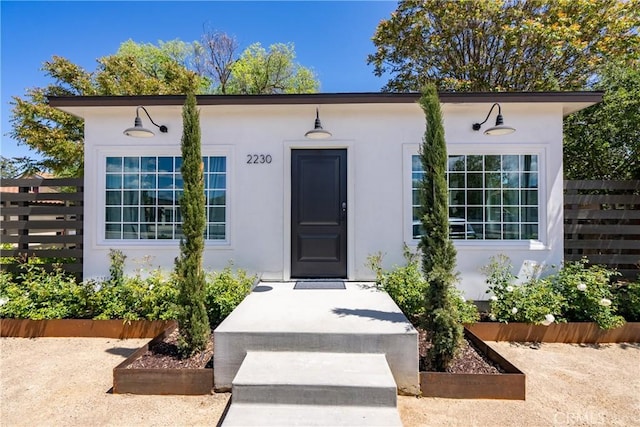 doorway to property featuring fence and stucco siding