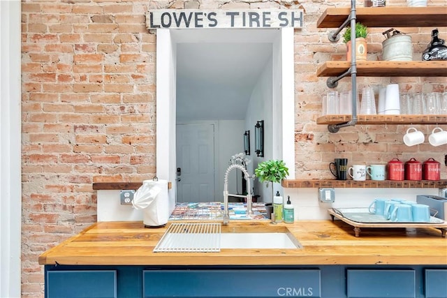 kitchen featuring blue cabinetry, brick wall, wood counters, and a sink