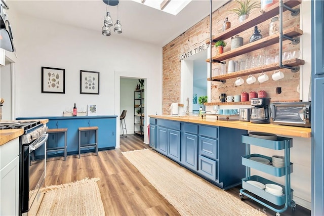 kitchen featuring butcher block countertops, blue cabinetry, light wood-style flooring, brick wall, and stainless steel gas range