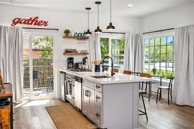 kitchen featuring pendant lighting, stainless steel appliances, light countertops, a sink, and light wood-type flooring