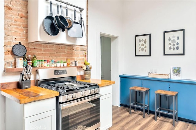 kitchen with light wood finished floors, wood counters, ventilation hood, white cabinetry, and gas stove