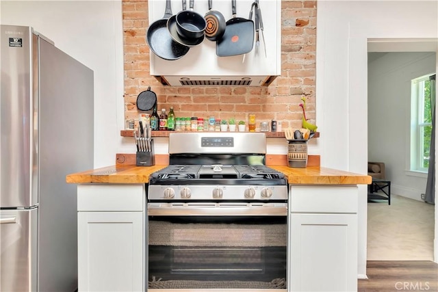 kitchen featuring stainless steel appliances, white cabinetry, wood counters, and ventilation hood