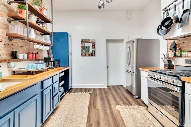 kitchen featuring stainless steel gas range oven, blue cabinets, wooden counters, light wood-type flooring, and open shelves