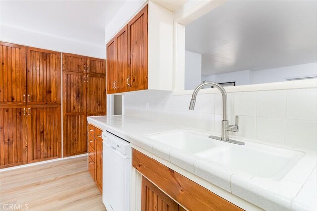 kitchen with decorative backsplash, dishwasher, sink, and light hardwood / wood-style flooring