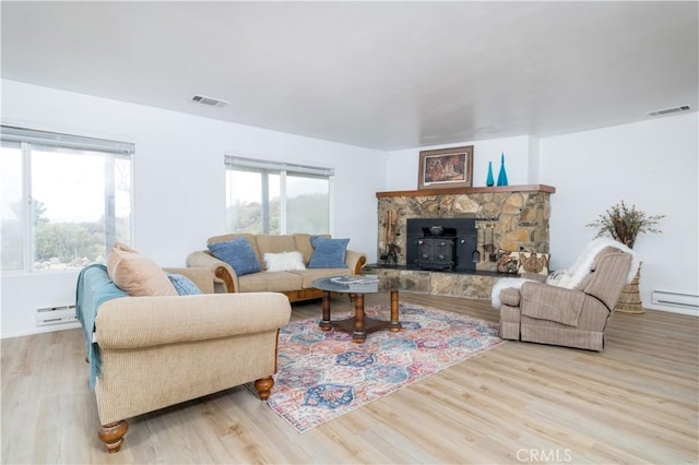 living room with baseboard heating, light hardwood / wood-style floors, a wood stove, and a wealth of natural light