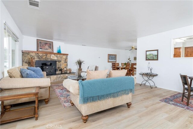 living room with ceiling fan, light hardwood / wood-style floors, and a wood stove