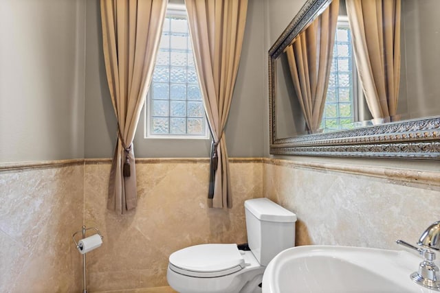 bathroom with a healthy amount of sunlight, toilet, sink, and tile walls