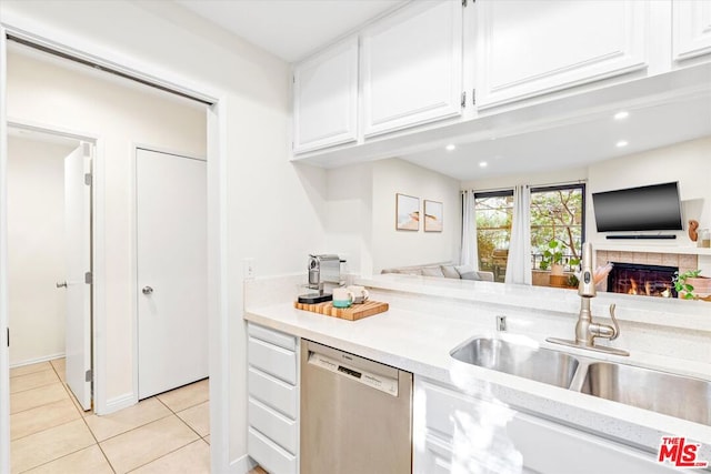 kitchen featuring white cabinets, stainless steel dishwasher, a fireplace, sink, and light tile patterned floors