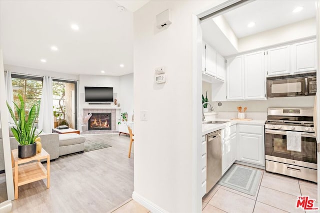 kitchen featuring white cabinets, appliances with stainless steel finishes, a fireplace, sink, and light tile patterned floors