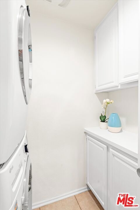 laundry area with cabinets, light tile patterned floors, and stacked washing maching and dryer