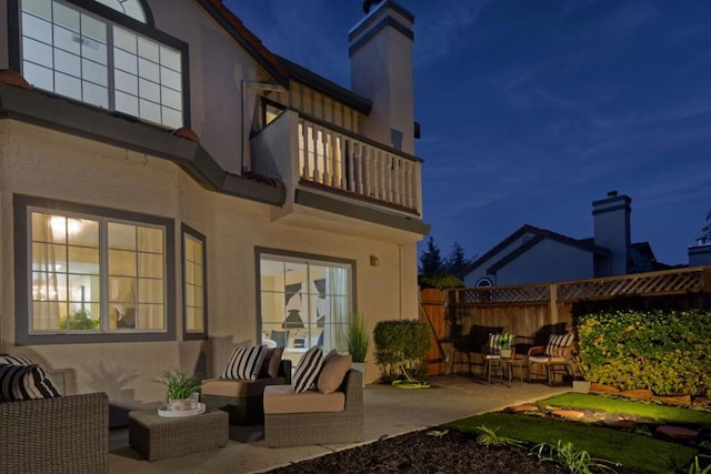 back house at night with a patio area, outdoor lounge area, and a balcony