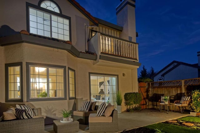 back house at twilight with a patio area, outdoor lounge area, and a balcony