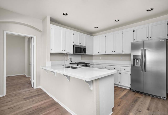 kitchen with white cabinets, kitchen peninsula, appliances with stainless steel finishes, and hardwood / wood-style floors