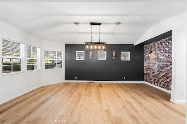 unfurnished dining area featuring vaulted ceiling, light hardwood / wood-style floors, and brick wall