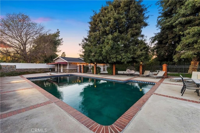 pool at dusk featuring a diving board and a patio