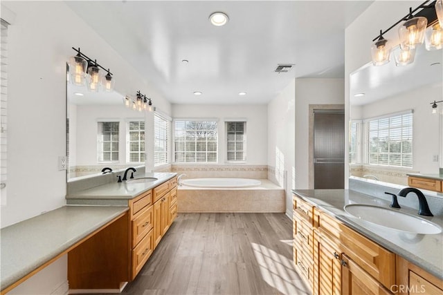 bathroom with hardwood / wood-style flooring, vanity, and tiled bath