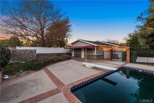 pool at dusk featuring a diving board and a patio area